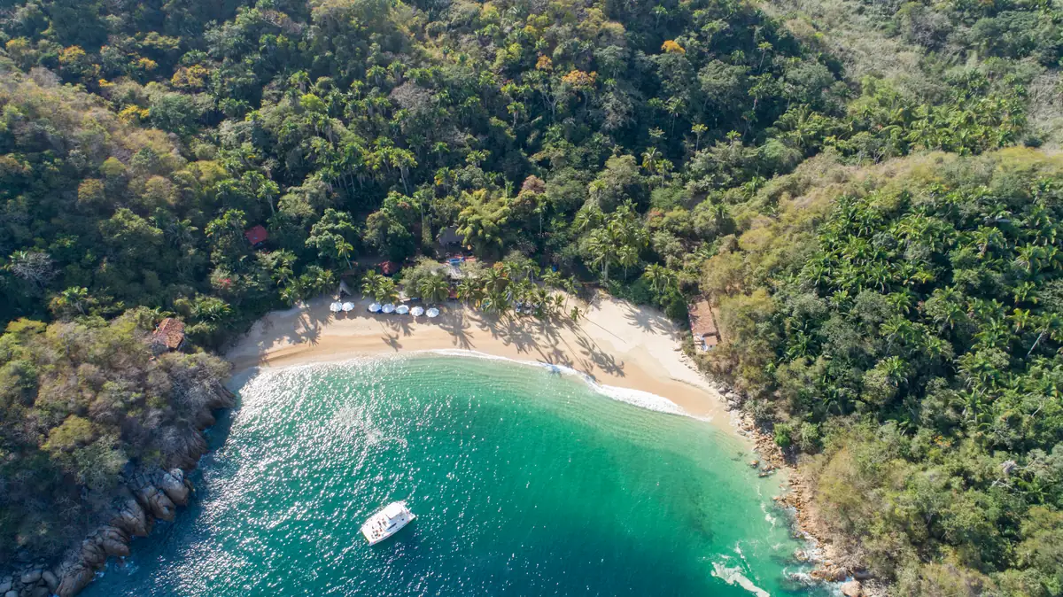 Aerial view of Majahuitas cove, showing the beach enclosed by jungle with a boat anchored in turquoise water