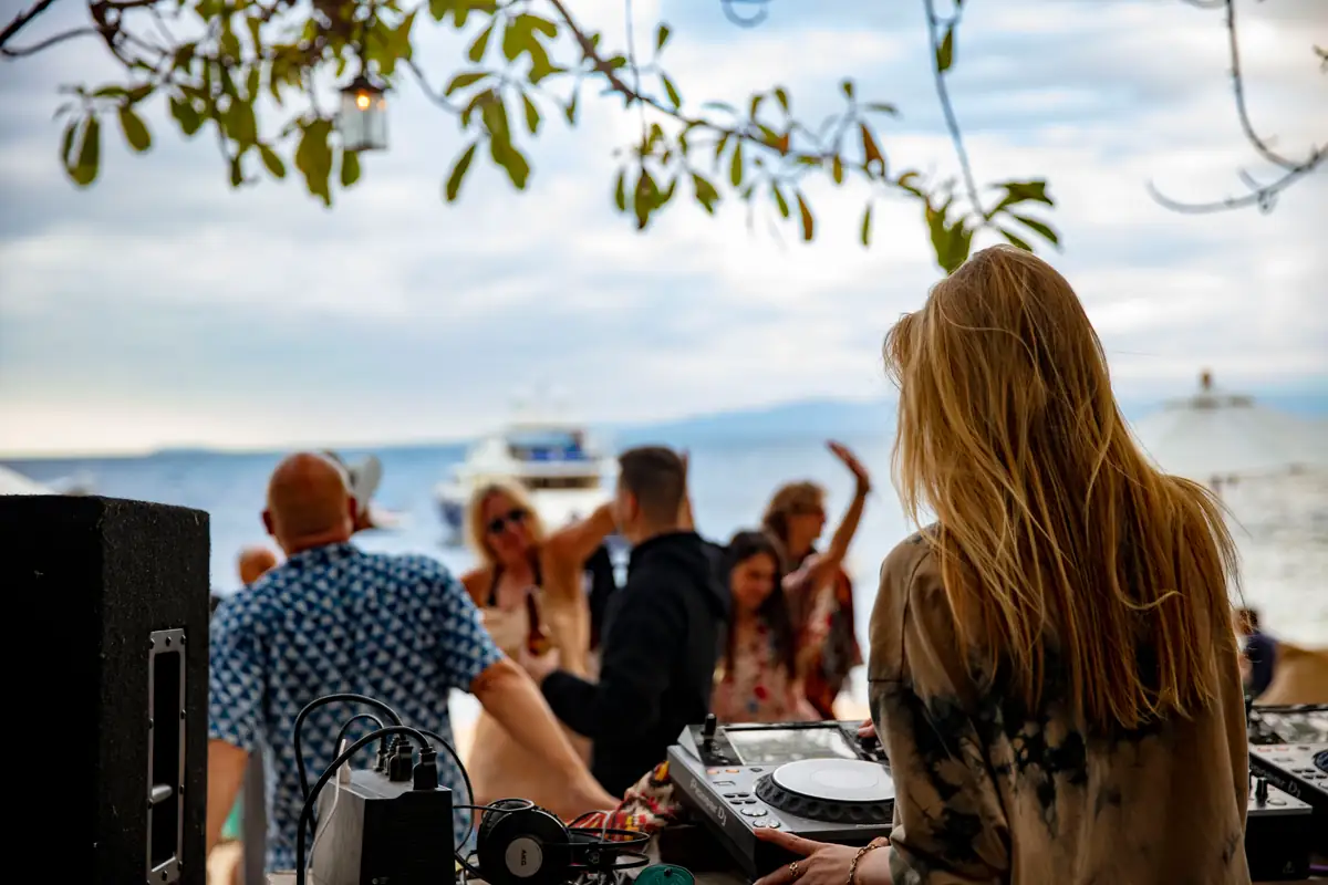 Guests dancing at the DJ booth on the sand at Majahuitas with the bay behind them